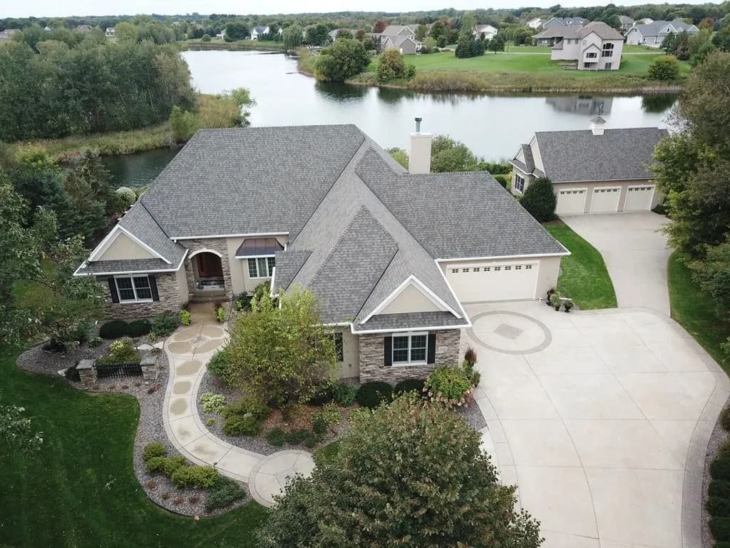 Aerial view of a two-story home beside a pond with a newly installed gray shingle roof