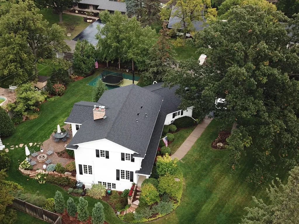 Aerial view of a repaired dark shingle roof on a white colonial home