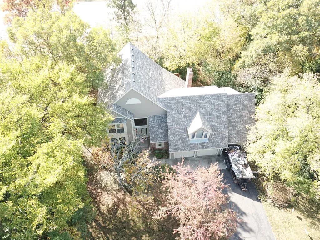 Aerial view of a home on a wooded lot with a new shingle roof and a rebuilt chimney flashing detail