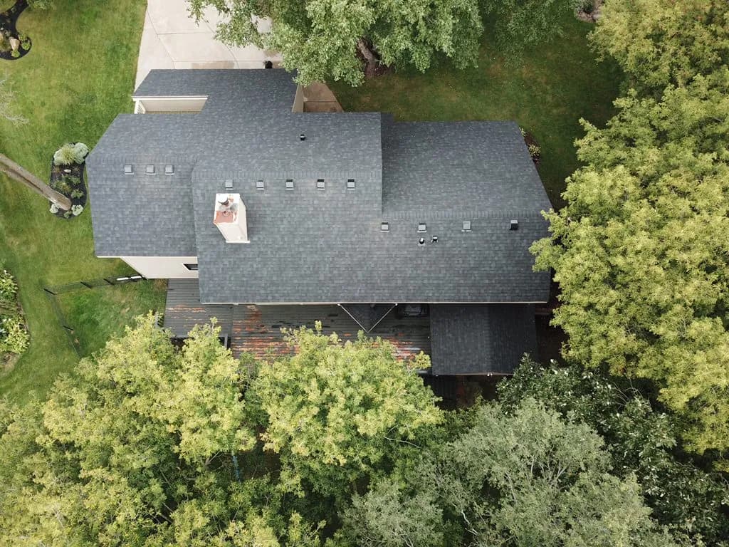 Aerial view of a home surrounded by woods with a new gray architectural shingle roof