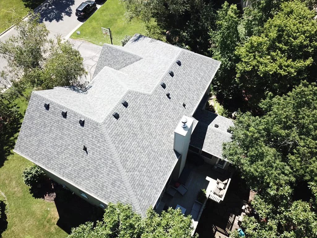 Aerial view of a new gray shingle roof on a house set into a wooded lot